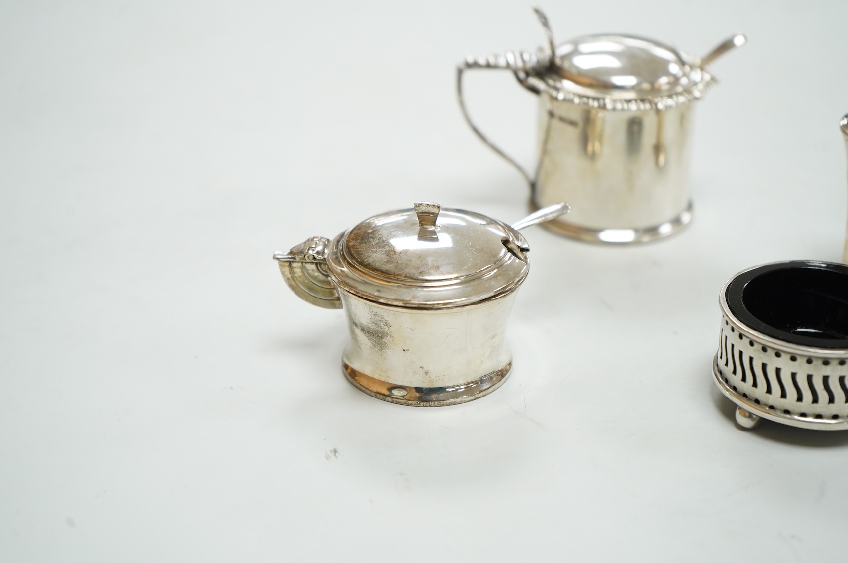 A George V Art Deco three piece silver condiment set and two spoons by William Adams Ltd, Birmingham, 1935, together with a pair of late Victorian pierced silver salts with blue glass liners and an Edwardian silver musta